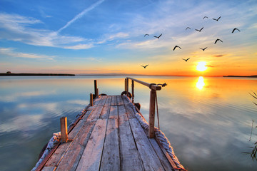 Fototapeta Bajeczny wschód słońca nad jeziorem z drewnianym pomostem obraz