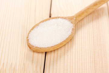 White sugar in spoon on wooden background