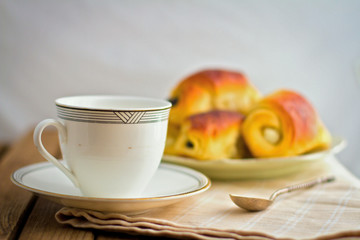 White cup and fresh buns on plate on wooden table