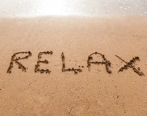Word Relax in handwriting on sandy beach