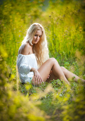 Fototapeta na wymiar Piękna blondynka w białej sukni siedzi w trawie