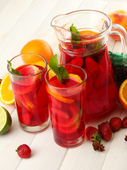 sangria in jar and glasses with fruits, on white wooden table