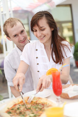 Young couple cutting pizza in cafe