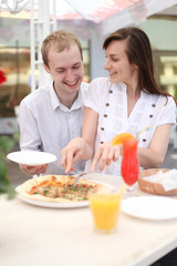 Young couple cutting pizza in cafe