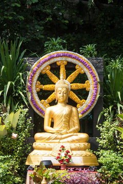 golden image of Buddha is sitting in front of Wheel of Dhamma