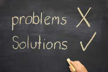 hand ticking the word solutions on a blackboard