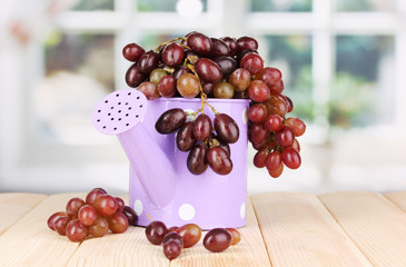 Ripe grapes in watering can on wooden table on window