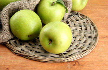 Ripe green apples with leaves on burlap, on wooden table