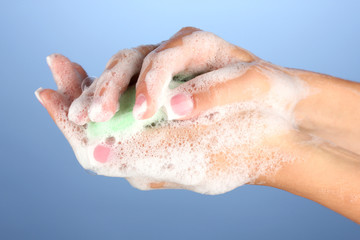Fototapeta premium Woman's hands in soapsuds, on blue background close-up