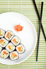 Sushi rolls on the plate with black chopsticks on green mat