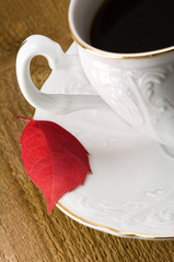 White cup with black coffee and red, autumn leaf