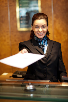 Cheerful female receptionist offering check-in papers
