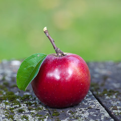 Красное яблоко на старом столе в саду.