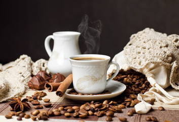 a cup of aromatic hot coffee, coffee beans, milk jug & cinnamon