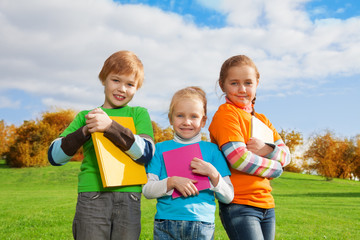 three kids with books in park
