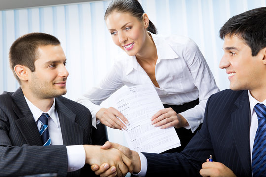 Three businesspeople handshaking with document