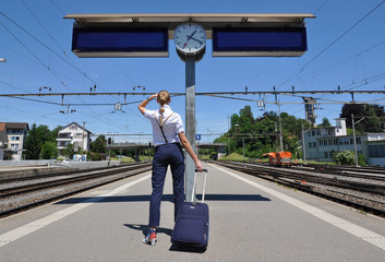 Girl with a suitcase looking at clock at the train station