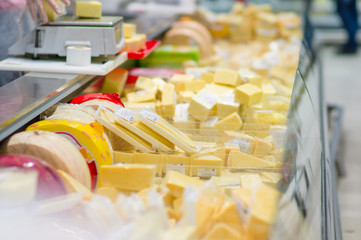 Pieces of different cheeses in fridge in supermarket