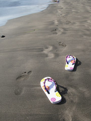 Fototapeta na wymiar Flip-flops on the black sand of Tenerife island, Canaries