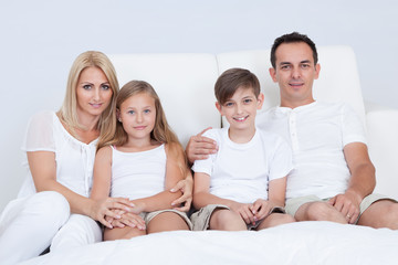 Portrait Of Happy Family Sitting On Bed