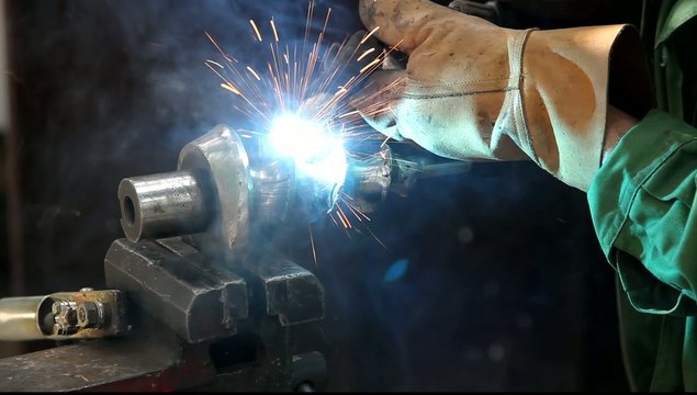 Welder doing arc welding of a steel shaft with helicoid