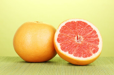 Ripe grapefruit and half on bamboo mat on green background