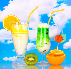 Delicious milk shakes with fruit on table on sky background