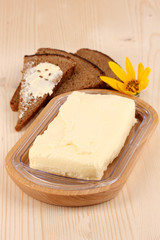 Butter on wooden holder and bread on wooden table close-up