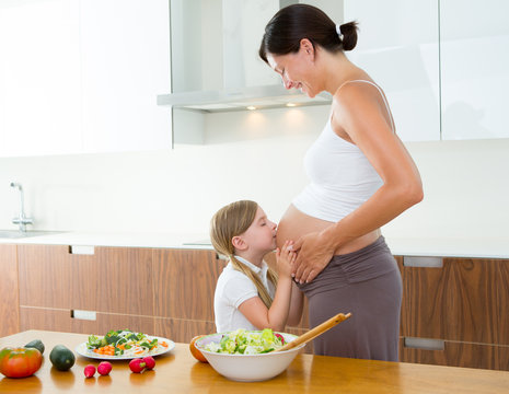 Beautiful pregnant mother with her daughter at kitchen