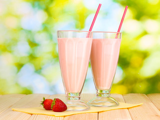 Strawberry milk shakes on wooden table on bright background
