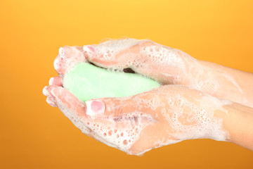 Woman's hands in soapsuds, on orange background close-up