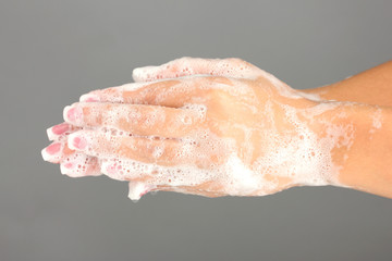 Woman's hands in soapsuds, on gray background close-up