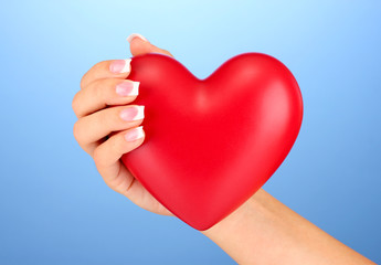 Obraz premium Red heart in woman's hand, on blue background close-up
