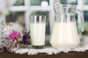 Pitcher and glass of milk on wooden table on window background