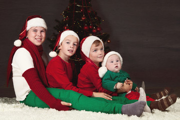 Four children sitting around Christmas tree.