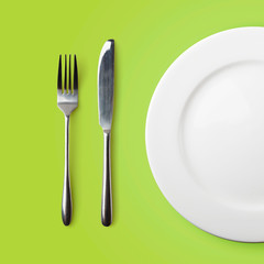 Empty plate, fork and knife on green background