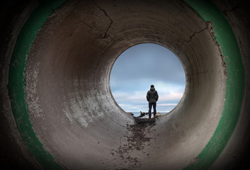 Man looks at horizon in the end of dark concrete tunnel - obrazy, fototapety, plakaty