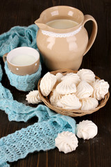 Pitcher and cup of milk with meringues on wooden table close-up