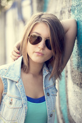 Teen girl in sunglasses near graffiti wall.
