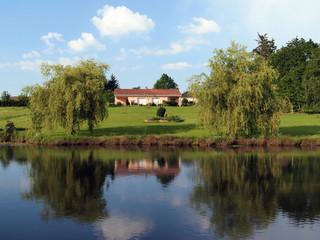 Landscape of a rural french property with a house reflected in the pond