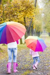 mother and her daughter with umbrellas in autumnal alley