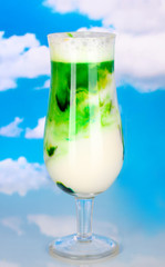 Delicious milk shake with fruit on table on sky background