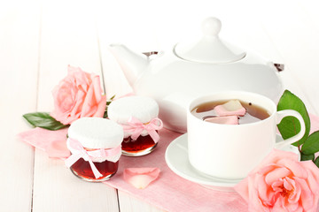 teapot and cup of tea with roses and jam on white wooden table