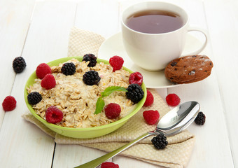tasty oatmeal with berries and cup of tea, on white wooden