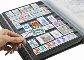 Hand holding postage stamp with tweezers over album - 45594393