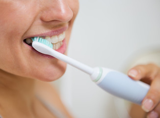 Closeup on woman brushing teeth with electric toothbrush