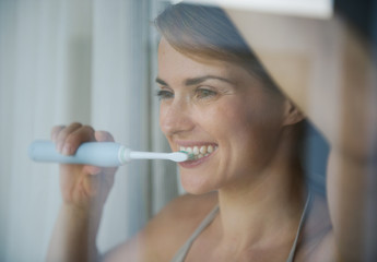 Young woman brushing teeth with electric toothbrush and looking