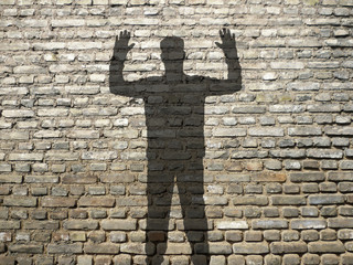 ombre d'homme mains en l'air, sur mur de briques
