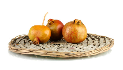 unripe pomegranates on wicker mat isolated on white