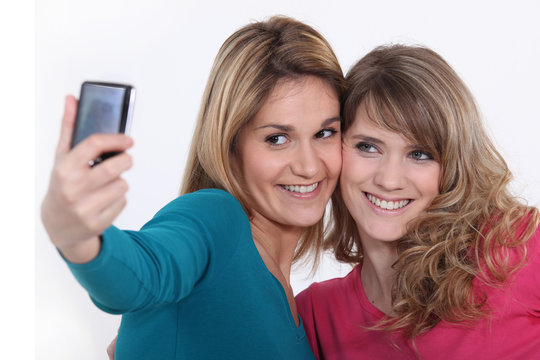 Two girls taking a picture with a mobile phone